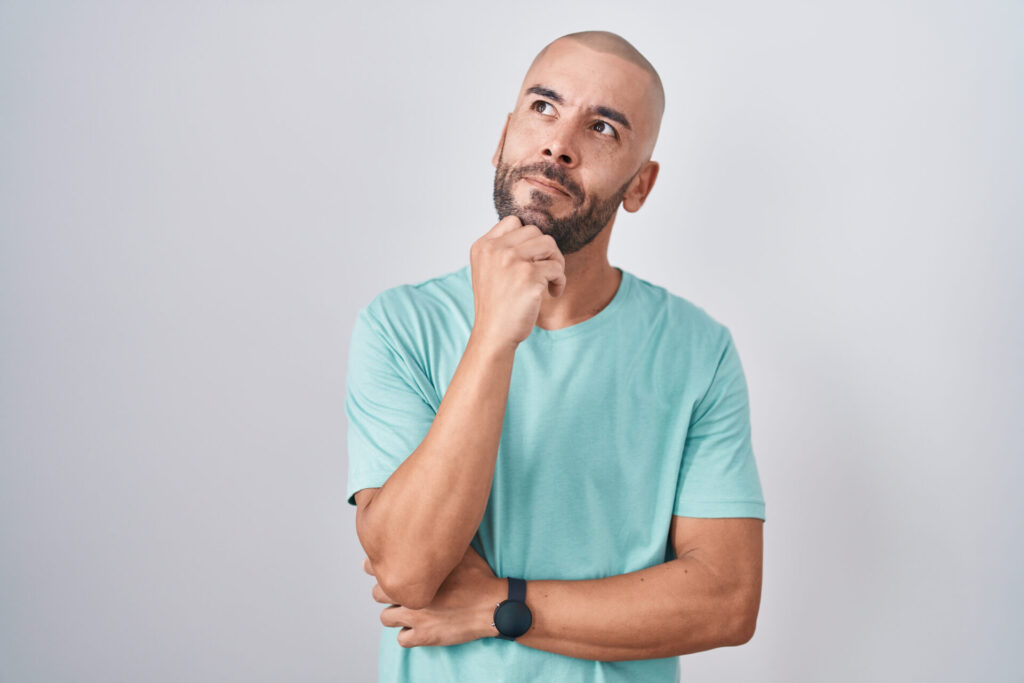 Middle age bald man standing over white background with hand on chin thinking about question, pensive expression. smiling with thoughtful face. doubt concept.